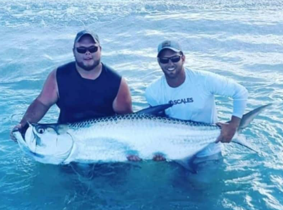 Two anglers holding a large tarpon in the water