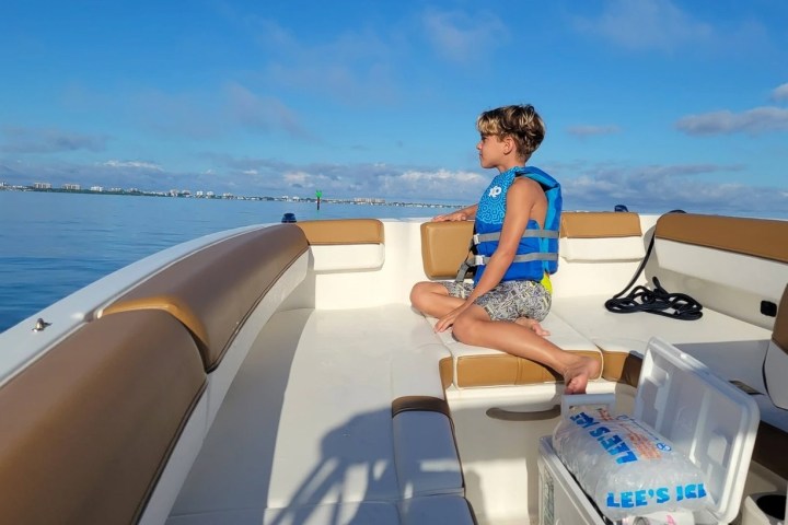 A boy on a boat looking at the ocean. Bayliner bowrider boat rental in Sarasota, FL, floating on calm, turquoise waters, ideal for family outings and versatile activities