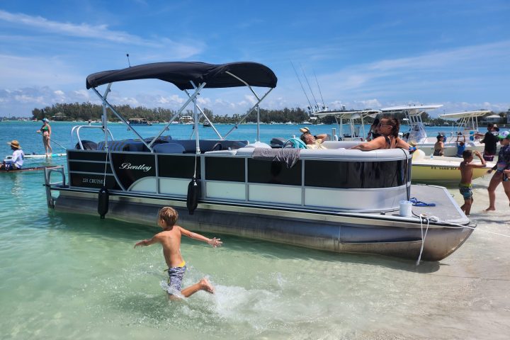 A 22-foot pontoon boat rental rests near the sandy beach of Beer Can Island, surrounded by calm waters and lush greenery