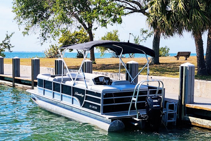 A 22-foot pontoon boat docked at Centennial Boat Ramp in Sarasota on a beautiful sunny day, with clear skies and calm waters inviting a perfect boating experience