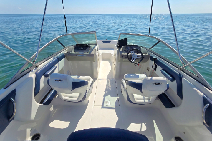 Interior of a small motorboat with two seats and a steering wheel, on calm blue water.