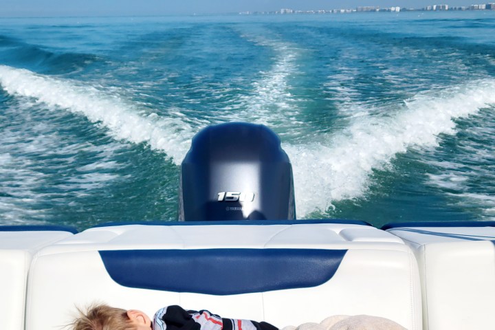 Child sleeping on a boat with a blue ocean and wake in the background.