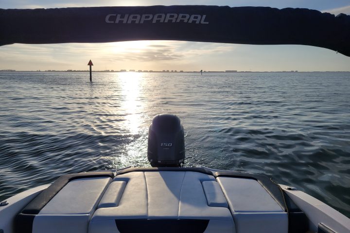 Boat deck facing sunset over calm water with distant marker buoy.