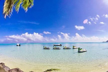 a group of people on a beach near a pretty body of water with jet ski rentals