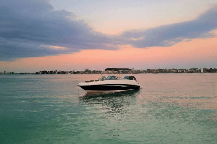 Boat on calm water at sunset with pink and orange sky, distant shoreline visible.